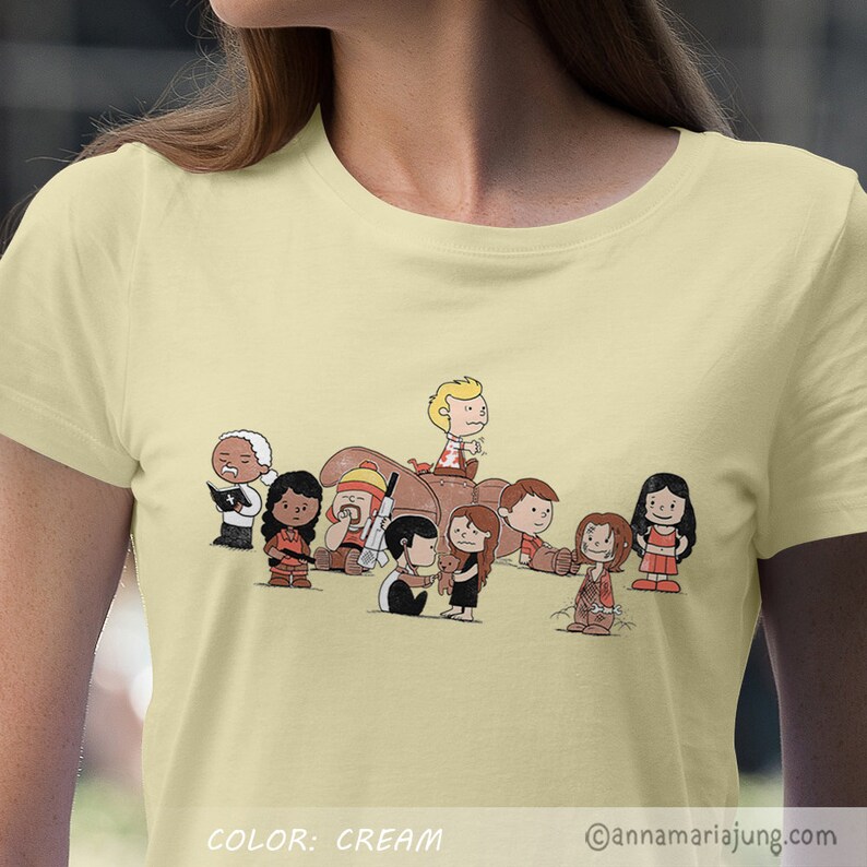 以下が含まれることがあります： クリーム色のTシャツに、映画「ゴーストバスターズ」のキャストに扮したピーナッツのキャラクターの漫画イラストが描かれています。シャツの下部に「COLOR: CREAM」の文字があります。