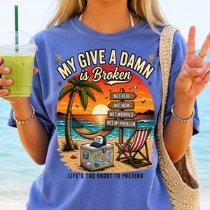 May include: A blue t-shirt featuring a graphic of a beach scene with a palm tree, a hammock, a cooler with a hat, and a beach chair. The text reads MY GIVE A DAMN is Broken, NOT HERE, NOT NOW, NOT WORRIED, NOT MY PROBLEM, and LIFE'S TOO SHORT TO PRETEND.