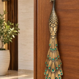 Peut inclure: Une poignée de porte verticale en forme de paon, fabriquée en métal couleur laiton antique. Le design présente des textures de plumes détaillées le long du corps et de la queue, agrémentées de cristaux vert émeraude en forme de goutte.