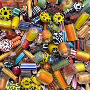 Puede incluir: Una gran colección de cuentas de vidrio variadas en diversas formas, tamaños y colores, incluyendo amarillo, naranja, verde, azul y negro, con patrones de rayas, florales y puntos, y orificios centrales visibles para ensartar.