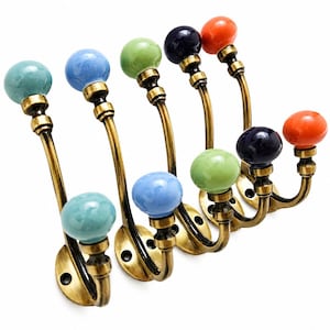 May include: A set of wall-mounted coat hooks featuring antique brass-finished metal arms and colorful ceramic ball finials. The hooks are arranged in a staggered formation, showcasing shades of light blue, green, dark blue, and bright orange.