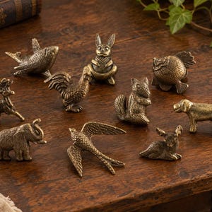 May include: A collection of ten small, antique-style brass animal figurines including a shark, a rabbit, a rooster, a squirrel, a fish, a deer, an elephant, a bird in flight, and a dog, all featuring detailed textures and a metallic finish.