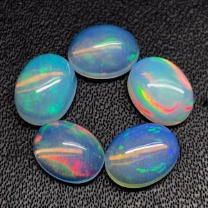 Puede incluir: Cinco ópalos cabujón de forma ovalada dispuestos en un patrón circular. Cada piedra preciosa presenta una base blanca lechosa y translúcida con destellos iridiscentes vibrantes, incluyendo juegos de colores en verde brillante, naranja y rojo.