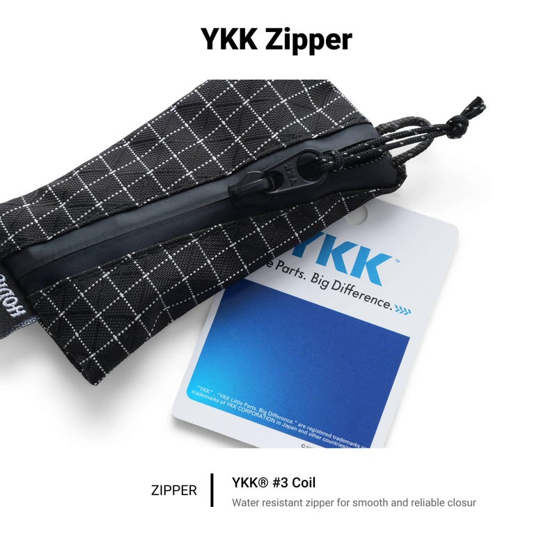 Pu&ograve; includere: Primo piano di una custodia a scacchi bianchi e neri con una cerniera nera. La cerniera &egrave; etichettata "YKK #3 Coil" ed &egrave; resistente all'acqua. L'immagine include anche un'etichetta con il logo "YKK" e il testo "Parts. Big Difference."