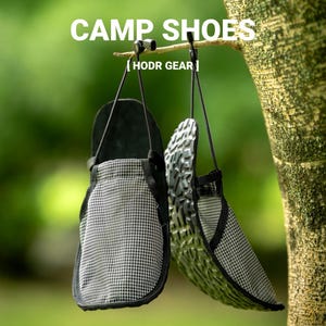 May include: A pair of black and white grid-patterned camp shoes with black trim and black soles, hanging from a tree branch. The shoes feature black drawstrings and are labeled with the text CAMP SHOES and HODR GEAR in white lettering.