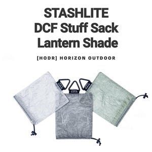 Könnte beinhalten: Drei DCF-Stoffsäcke und Laternen-Schirme in Weiß, Grau und Grün. Jeder Sack hat einen Kordelzugverschluss und einen schwarzen Karabiner. Der Text "STASHLITE DCF Stuff Sack Lantern Shade" steht oben.