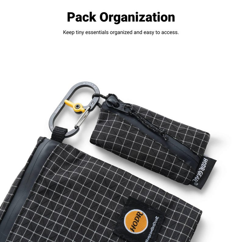 Pu&ograve; includere: Due pochette a scacchi bianchi e neri con un moschettone. Le pochette hanno una chiusura a cerniera e una piccola etichetta con la scritta "HODR GEAR". &Egrave; visibile anche il testo "Pack Organization" e "Keep tiny essentials organized and easy to access".