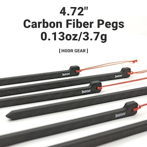 May include: A set of black carbon fiber pegs with red pull cords, each measuring 4.72 inches in length and weighing 0.13 ounces. The pegs feature the text HODR GEAR and the brand name HODR printed on the side of each individual unit.
