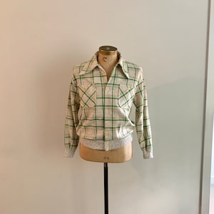 May include: A cream and green plaid long-sleeve shirt with a button-up front and two chest pockets. The shirt has a ribbed knit trim at the cuffs and waistband.