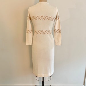May include: A white knitted dress with a brown geometric pattern. The dress has long sleeves and a fitted silhouette.
