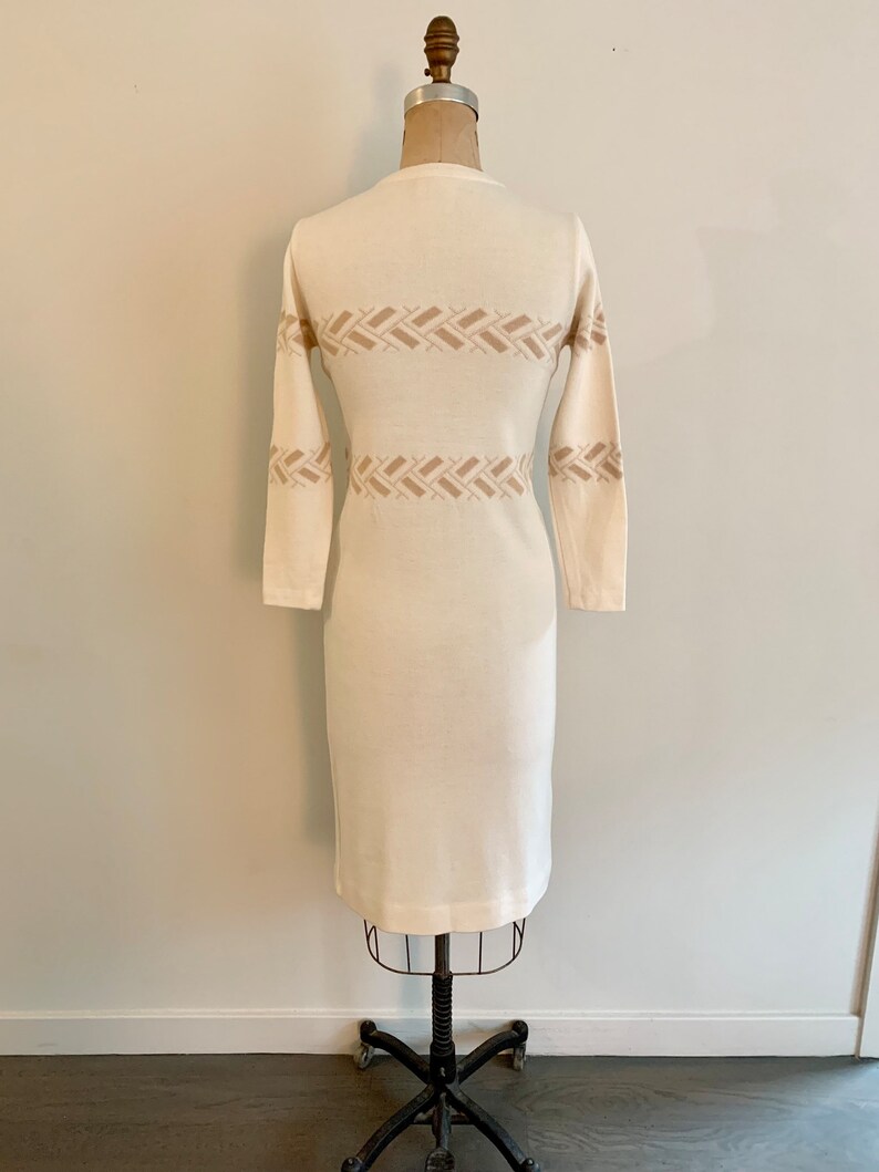 May include: A white knitted dress with a brown geometric pattern. The dress has long sleeves and a fitted silhouette.
