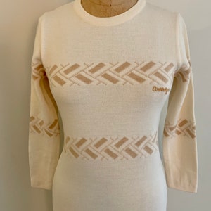 May include: A white long-sleeved sweater dress with a brown geometric pattern and the word "Courreges" on the front.