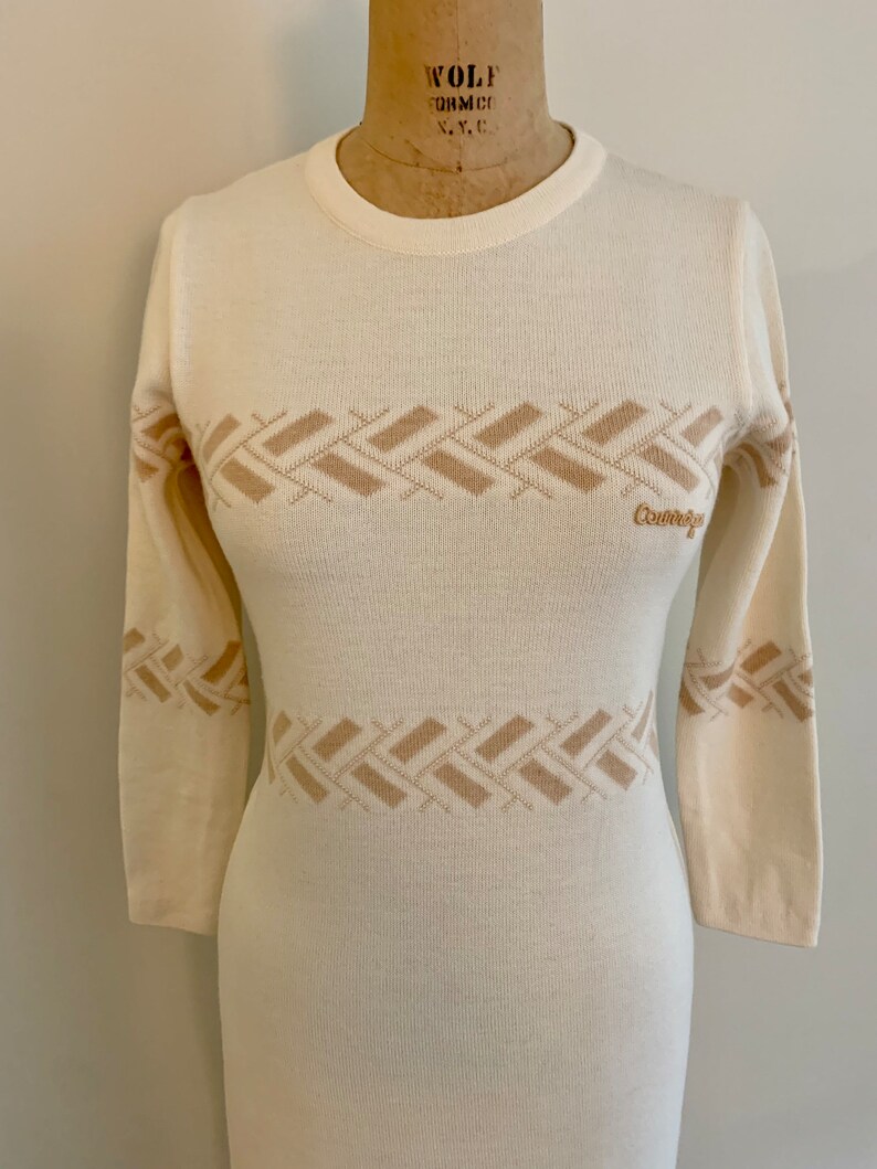 May include: A white long-sleeved sweater dress with a brown geometric pattern and the word "Courreges" on the front.