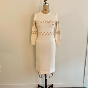 May include: A white long-sleeved sweater dress with a brown geometric pattern around the waist. The dress is on a white mannequin.