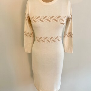 May include: A white long-sleeved sweater dress with a brown geometric pattern and the word "Couturier" embroidered on the front.