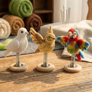 May include: Three needle-felted bird figures mounted on metal springs and round wooden bases. The set includes a solid white bird, a yellow bird with spread wings, and a multi-colored parrot with red, blue, green, and yellow plumage.