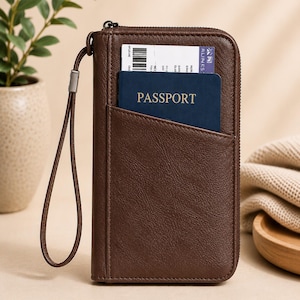 Könnte beinhalten: Braunes Reise-Portemonnaie aus Leder mit Reißverschluss, Handschlaufe und Fronttasche. Ein Reisepass und eine Bordkarte sind im Inneren sichtbar. Das Portemonnaie ist für Reisedokumente konzipiert.