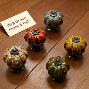 May include: Five colorful ceramic cabinet knobs in pumpkin shapes with bronze-colored hardware. The knobs are in shades of blue, orange, yellow, green, and brown. The text "diy & Drawer Knobs & Pulls" is on a white card.