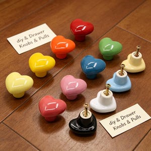 May include: A collection of heart-shaped ceramic drawer knobs in various colors including red, orange, yellow, green, blue, pink, white, and black. Each knob features a metal screw on the back. Two white cards are labeled "diy & Drawer Knobs & Pulls".
