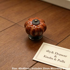 Pode incluir: Puxador decorativo para arm&aacute;rio com design de ab&oacute;bora, principalmente laranja e castanho, com centro de metal escuro. O texto no cart&atilde;o diz "diy & Drawer & Knobs & Pulls". O puxador mede 4 cm x 4 cm.