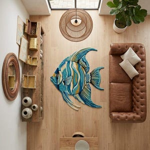 May include: A decorative fish-shaped rug in shades of blue, yellow, and white, placed on a wooden floor. The room features a brown leather sofa, a wooden shelf, and a woven light fixture. The rug's dimensions are approximately 180 cm.
