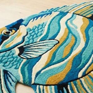 May include: A colourful fish-shaped rug with a vibrant design. The rug features shades of blue, teal, yellow, and white, creating a wave-like pattern across the body. The fish has detailed fins and a textured surface, adding depth to the decorative floor covering.