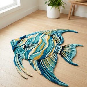 May include: A fish-shaped rug with a detailed design in shades of blue, yellow, and cream. The rug is placed on a wooden floor. The rug's dimensions are approximately 150 cm in length, offering a decorative marine theme for any room.