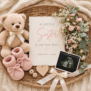 May include: A beige teddy bear with a cream ribbon, a pair of light pink knitted baby booties, a wooden heart, two wooden beads, a bouquet of baby's breath and eucalyptus, and an ultrasound photo next to a card reading A LITTLE Sister IS ON THE WAY! ARRIVING n. 202X.
