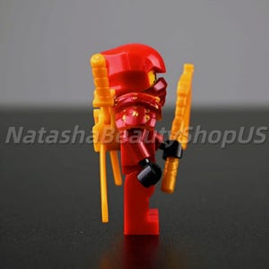 May include: A red and gold action figure with a helmet, armor, and two gold weapons. The figure is a ninja warrior. The text "NatashaBeautyShopUS" is visible on the left side of the image.