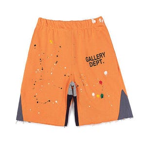 May include: Orange shorts with paint splatter details and the text "GALLERY DEPT." in black. The shorts have a raw hem and grey panels on the sides. The shorts are made of a soft material.