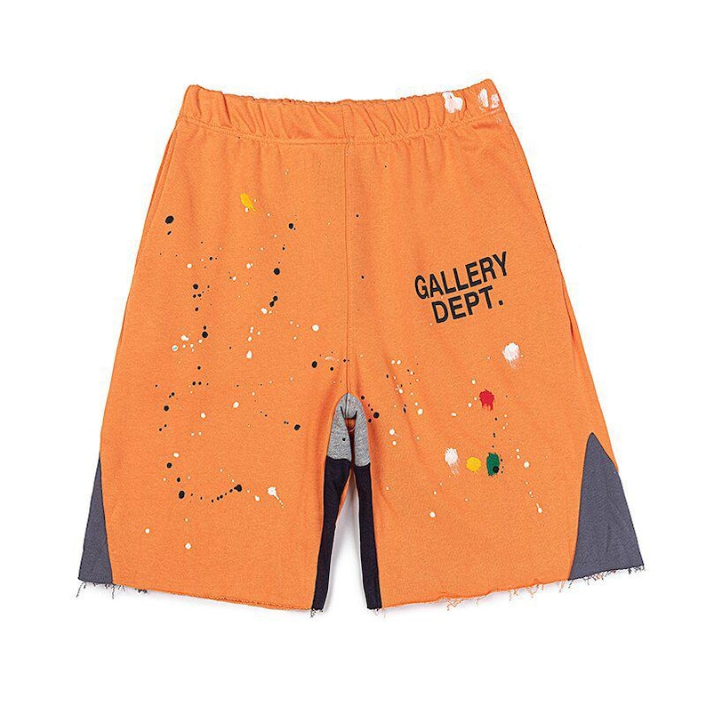 May include: Orange shorts with paint splatter details and the text "GALLERY DEPT." in black. The shorts have a raw hem and grey panels on the sides. The shorts are made of a soft material.