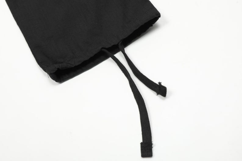 Puede incluir: Primer plano de tela negra con cierre de cord&oacute;n. La tela parece ser un material suave. Dos cordones negros se extienden desde la abertura, con un trozo rectangular al final de un cord&oacute;n.