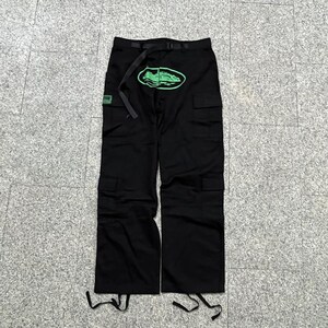 Puede incluir: Pantalones cargo negros con m&uacute;ltiples bolsillos y cintur&oacute;n. Un gr&aacute;fico ovalado verde con un dise&ntilde;o de zapato est&aacute; en la parte delantera. Un peque&ntilde;o parche cuadrado verde est&aacute; en el lado izquierdo. Los pantalones tienen cordones en la parte inferior.