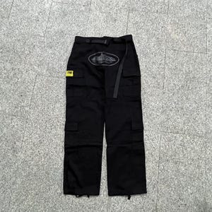 Puede incluir: Pantalones cargo negros con m&uacute;ltiples bolsillos y cintur&oacute;n. Los pantalones tienen un logotipo en la parte delantera y una peque&ntilde;a etiqueta amarilla. Fabricados con un material duradero, adecuados para diversas actividades.