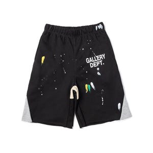 May include: Black shorts with white paint splatters and grey side panels. The text "GALLERY DEPT." is printed in white on the right leg. The shorts have an elasticated waistband and a drawstring.