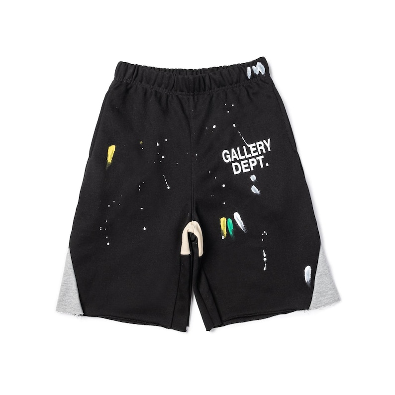 May include: Black shorts with white paint splatters and grey side panels. The text "GALLERY DEPT." is printed in white on the right leg. The shorts have an elasticated waistband and a drawstring.