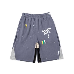 May include: Grey athletic shorts with paint splatter details and the text "GALLERY DEPT." in white. The shorts have grey and black side panels and a drawstring waistband. A casual, streetwear style.