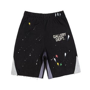 May include: Black athletic shorts with white paint splatter details and grey side panels. The shorts feature the text "GALLERY DEPT." in white on the right leg. The shorts have a raw hem.