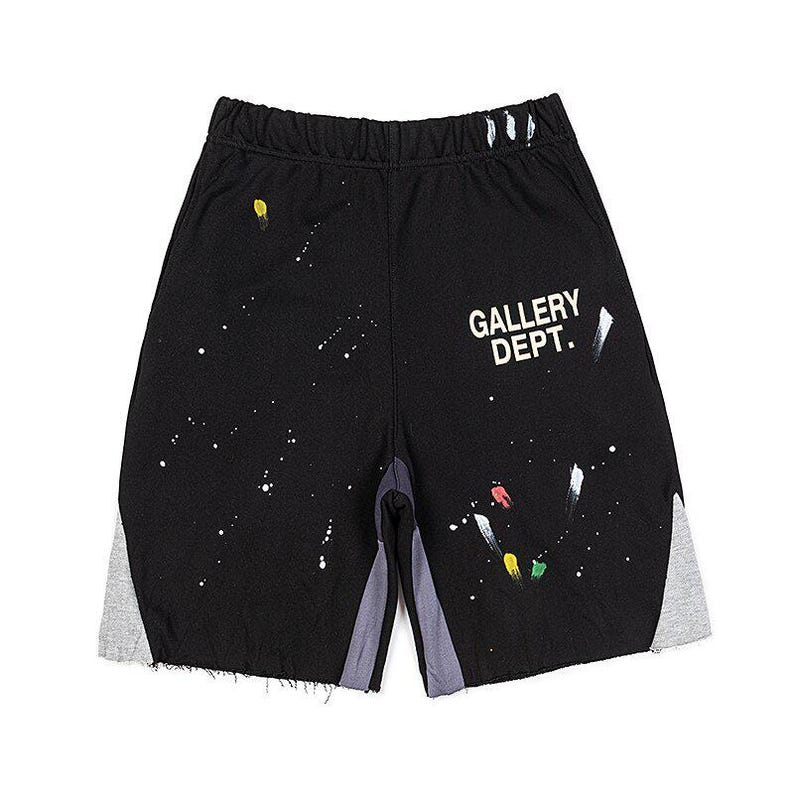 May include: Black athletic shorts with white paint splatter details and grey side panels. The shorts feature the text "GALLERY DEPT." in white on the right leg. The shorts have a raw hem.