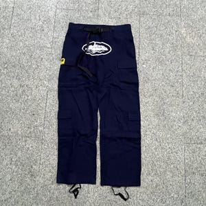 Puede incluir: Pantalones cargo azul marino con cintur&oacute;n negro y logotipo blanco. Los pantalones tienen m&uacute;ltiples bolsillos y cordones en los tobillos. Se ve un parche amarillo en el lado izquierdo.