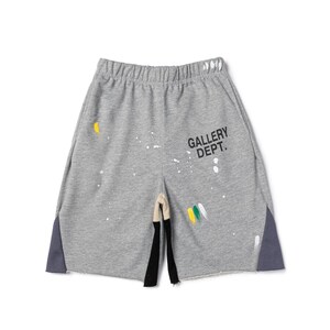 May include: Grey sweat shorts with paint splatter details and the text "GALLERY DEPT." The shorts have a raw hem, a drawstring waistband, and dark grey side panels. Paint colours include yellow, white, and green.