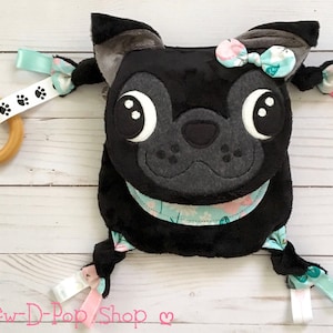 May include: Black and gray plush dog toy with a pink bow and a wooden teething ring. The toy has multiple fabric textures and a floral pattern.