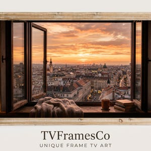 Puede incluir: Un marco de madera rectangular que rodea una pantalla digital con la vista de una ventana abierta hacia un horizonte urbano al atardecer. En el alféizar hay una manta de punto beige, una taza marrón y dos libros. El texto dice TVFramesCo.