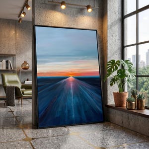 Könnte beinhalten: Große, gerahmte Leinwandkunst mit einem Sonnenuntergang über einer langen, blauen Straße. Das Kunstwerk hat einen schwarzen Rahmen und wird in einem modernen Innenraum ausgestellt. Der Himmel wechselt von Blau zu Orange und Rot.