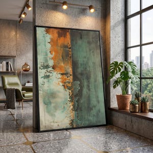 May include: Large framed abstract art print with a black frame. The artwork features a textured design with shades of teal, orange, and green. The artwork is leaning against a concrete wall in a modern interior setting.