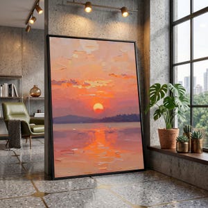 Könnte beinhalten: Gerahmtes Landschaftsgemälde mit Sonnenuntergang über dem Wasser. Das Kunstwerk verwendet Orange-, Gelb- und Lilatöne, wobei sich die Sonne auf dem Wasser spiegelt. Das Gemälde wird in einem modernen Innenraum ausgestellt.