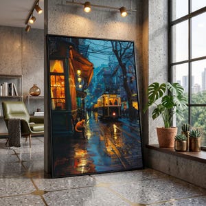 May include: A framed art print depicts a rainy street scene with a vintage tram, illuminated shop fronts, and a cat. The artwork features a palette of blues, oranges, and yellows, creating a warm, inviting atmosphere. The print is displayed in a modern interior setting.