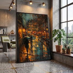 May include: A framed rectangular wall art print depicting a rainy city street scene at night with warm golden streetlights reflecting on wet pavement, silhouettes of people holding umbrellas, and dark trees under a moody, atmospheric sky.