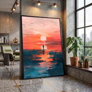 Pode incluir: Impressão artística emoldurada retratando uma silhueta em frente a um pôr do sol. A obra de arte utiliza cores laranja, vermelho e azul, com um grande sol e seu reflexo na água. A impressão é apresentada em uma moldura preta.