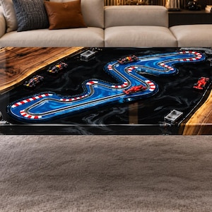 Op de afbeelding: Een rechthoekige salontafel met een rand van onbewerkt hout en een centraal inlegwerk van zwarte hars. Het harsoppervlak toont een gedetailleerd miniatuur Formule 1-circuit met blauwe baandelen en rood-witte randen met kleine racewagens.